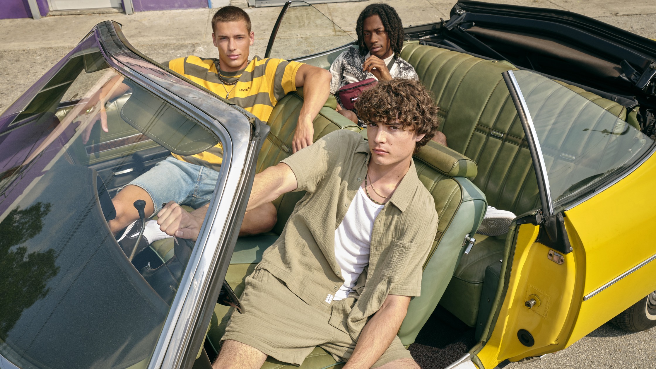 three young men sitting in the back of a yellow convertible car