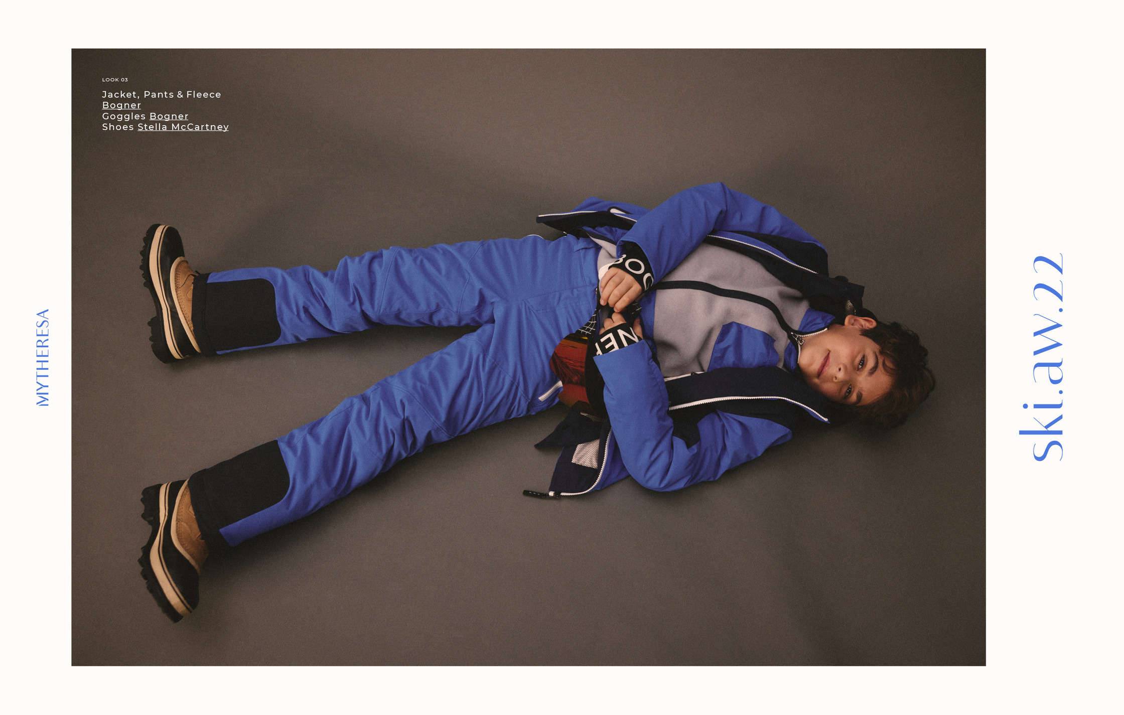 a young boy laying on the ground in a blue ski suit