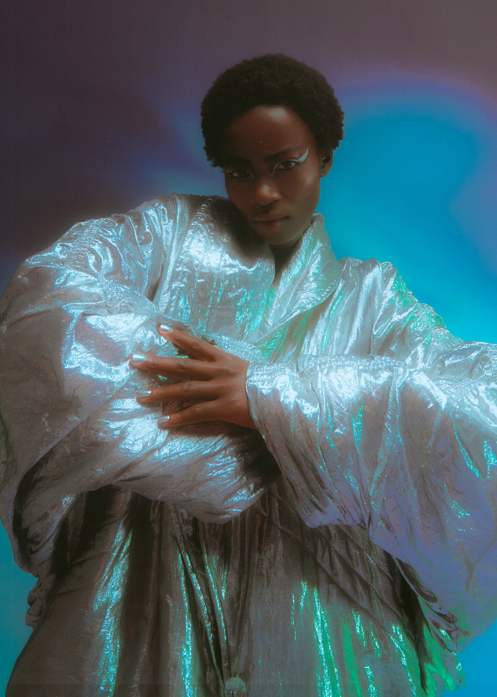 a woman in a silver coat posing in front of a blue background