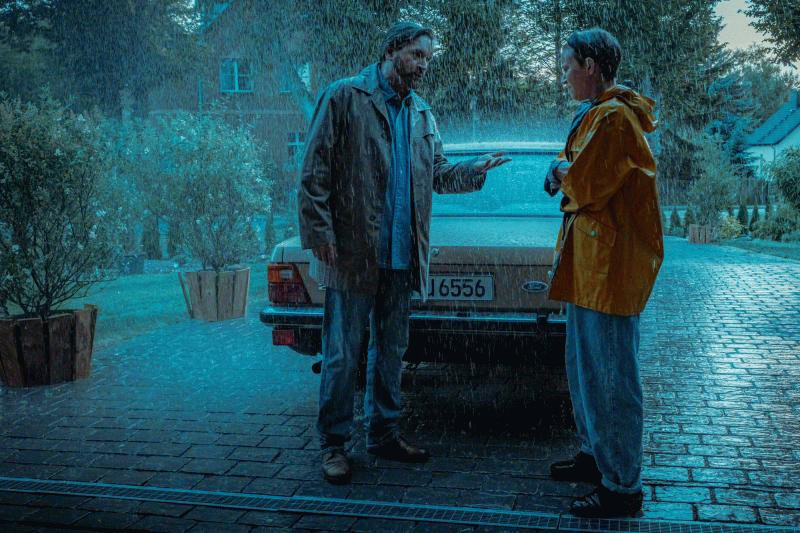 two men standing next to a car in the rain