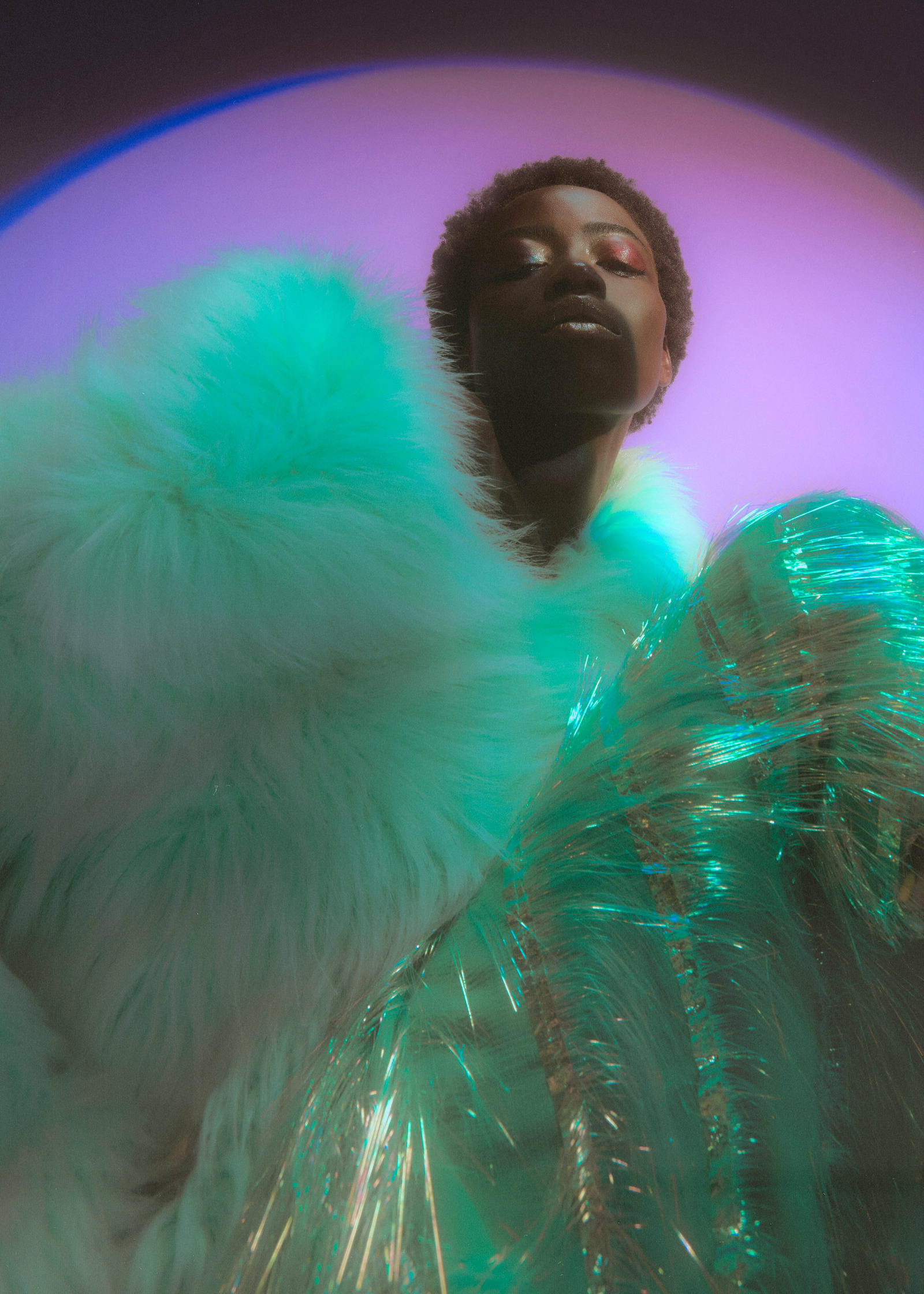 a woman in a green fur coat posing in front of a circular light