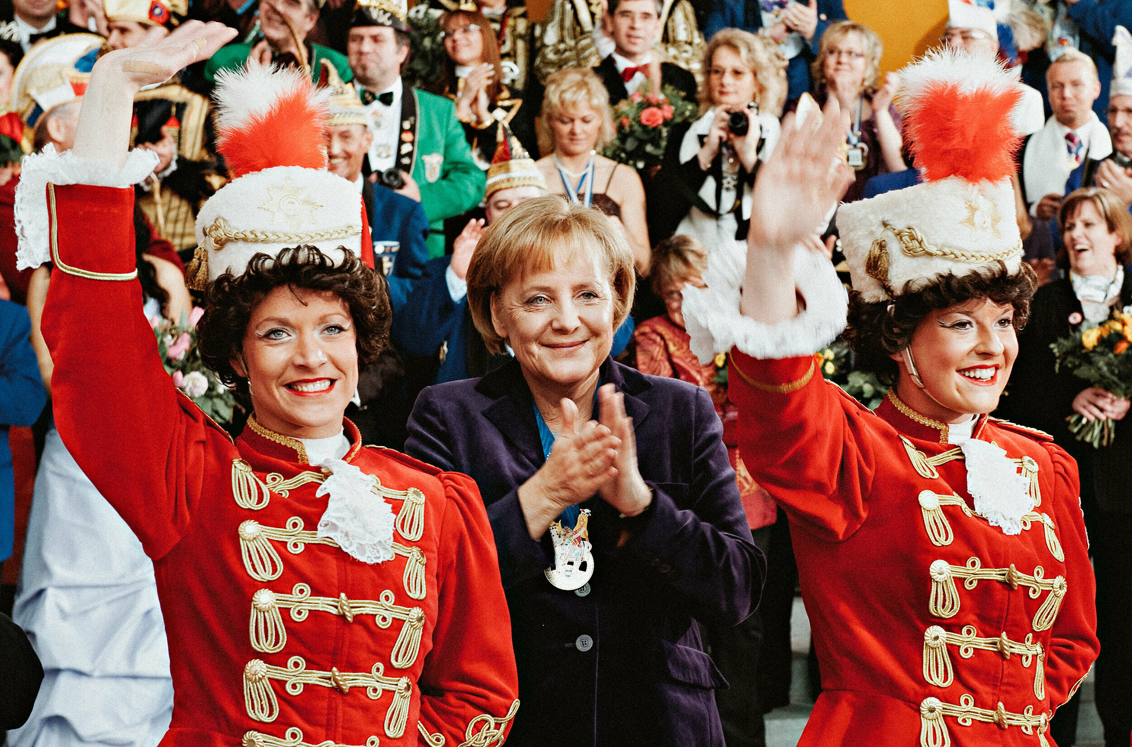 a group of women in red uniforms waving to the crowd angela merkel