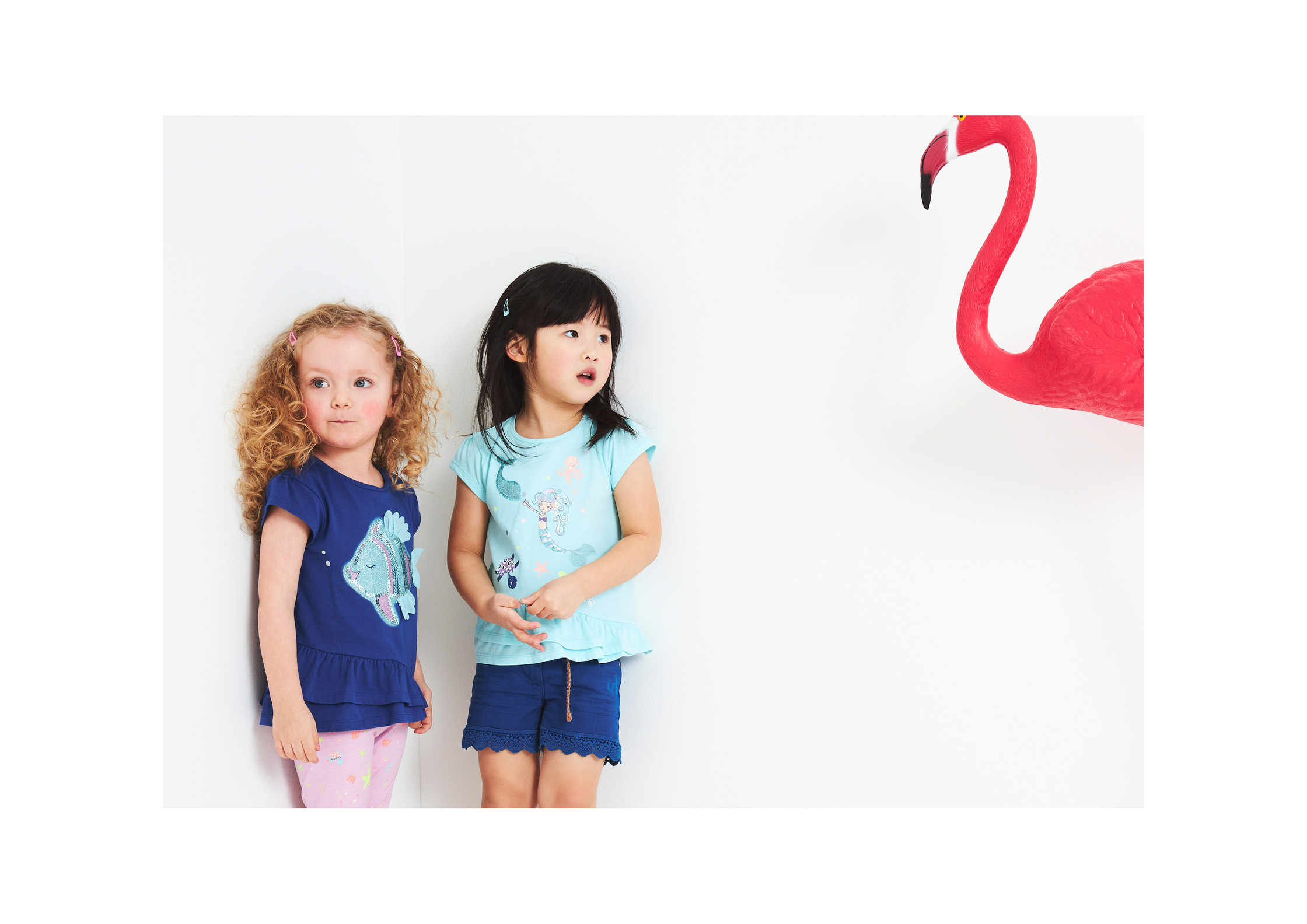 two little girls standing next to a pink flamingo