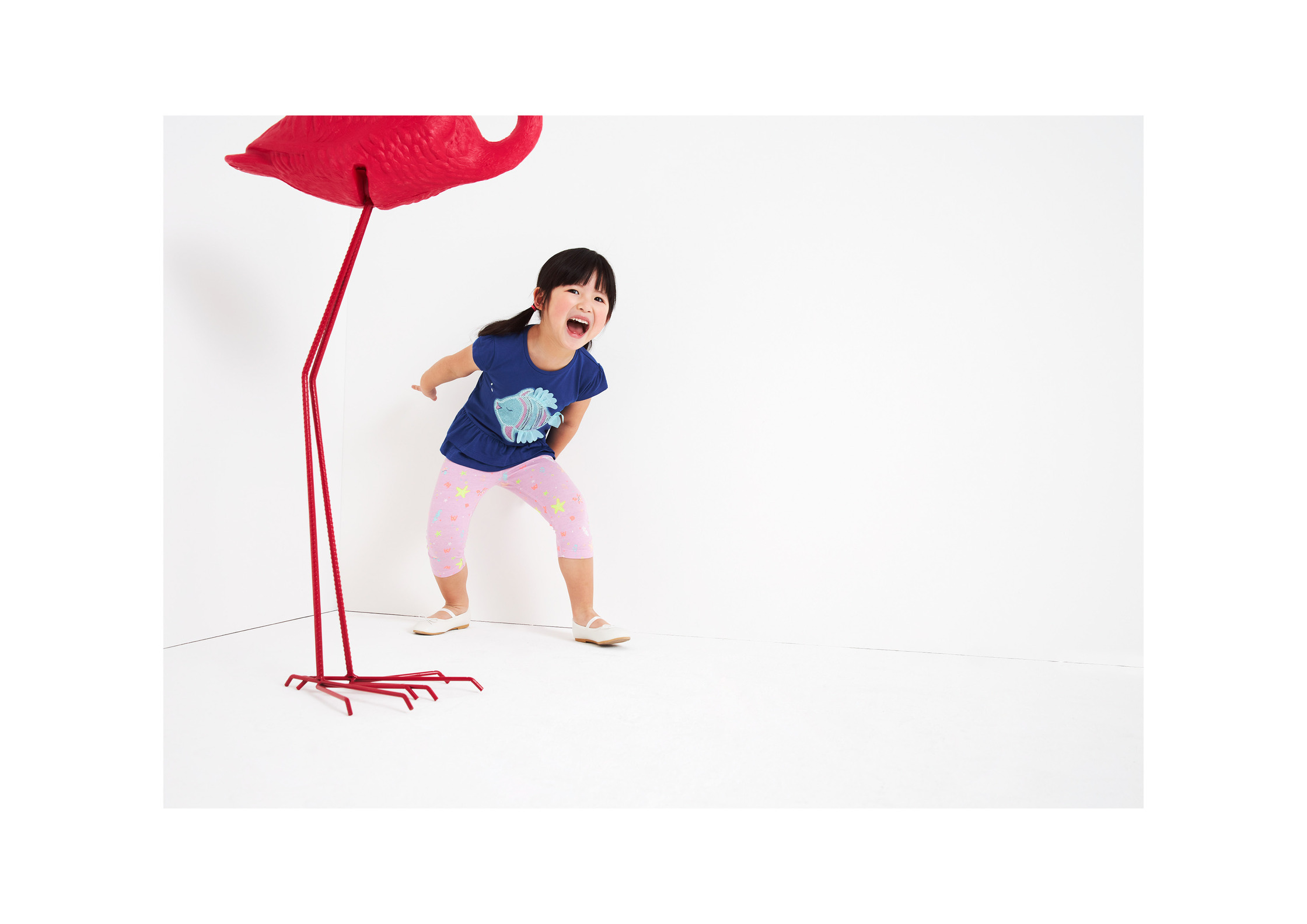 a little girl standing next to a red flamingo
