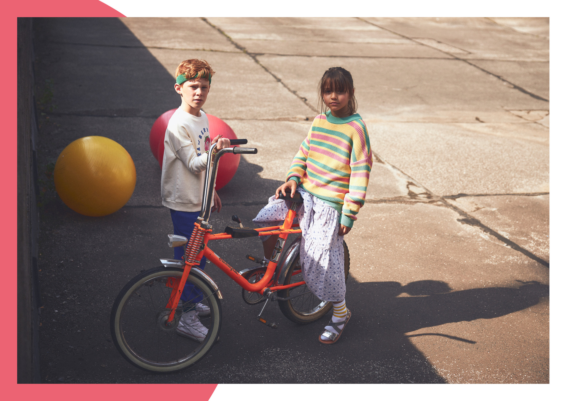 two kids standing next to a bicycle with balloons in the background