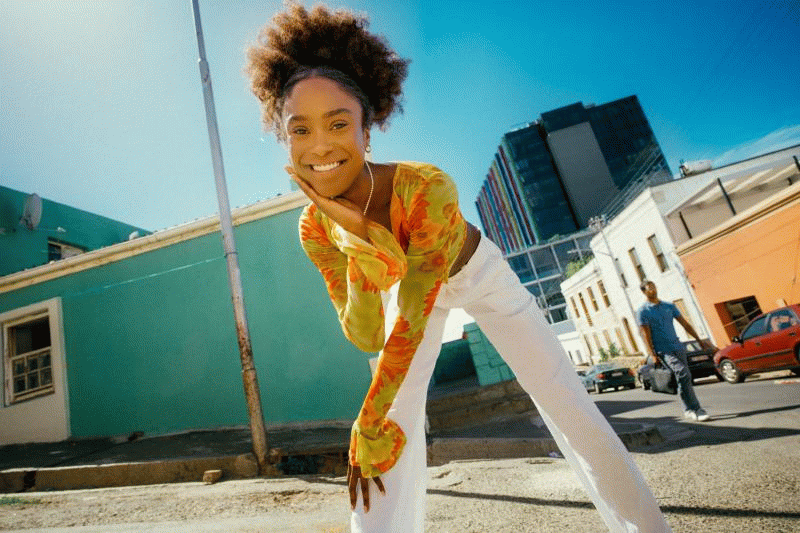 a woman in a yellow top and white pants standing on a street in cape town