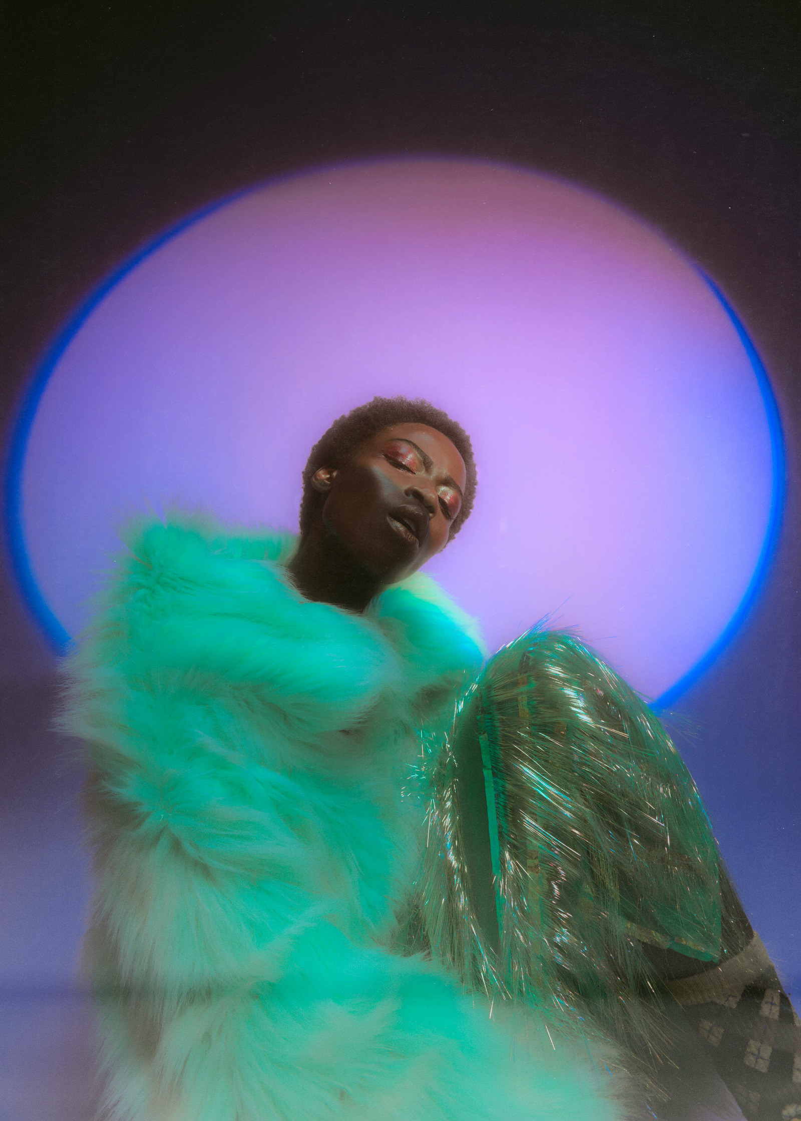 a woman in a green fur coat posing in front of a blue light