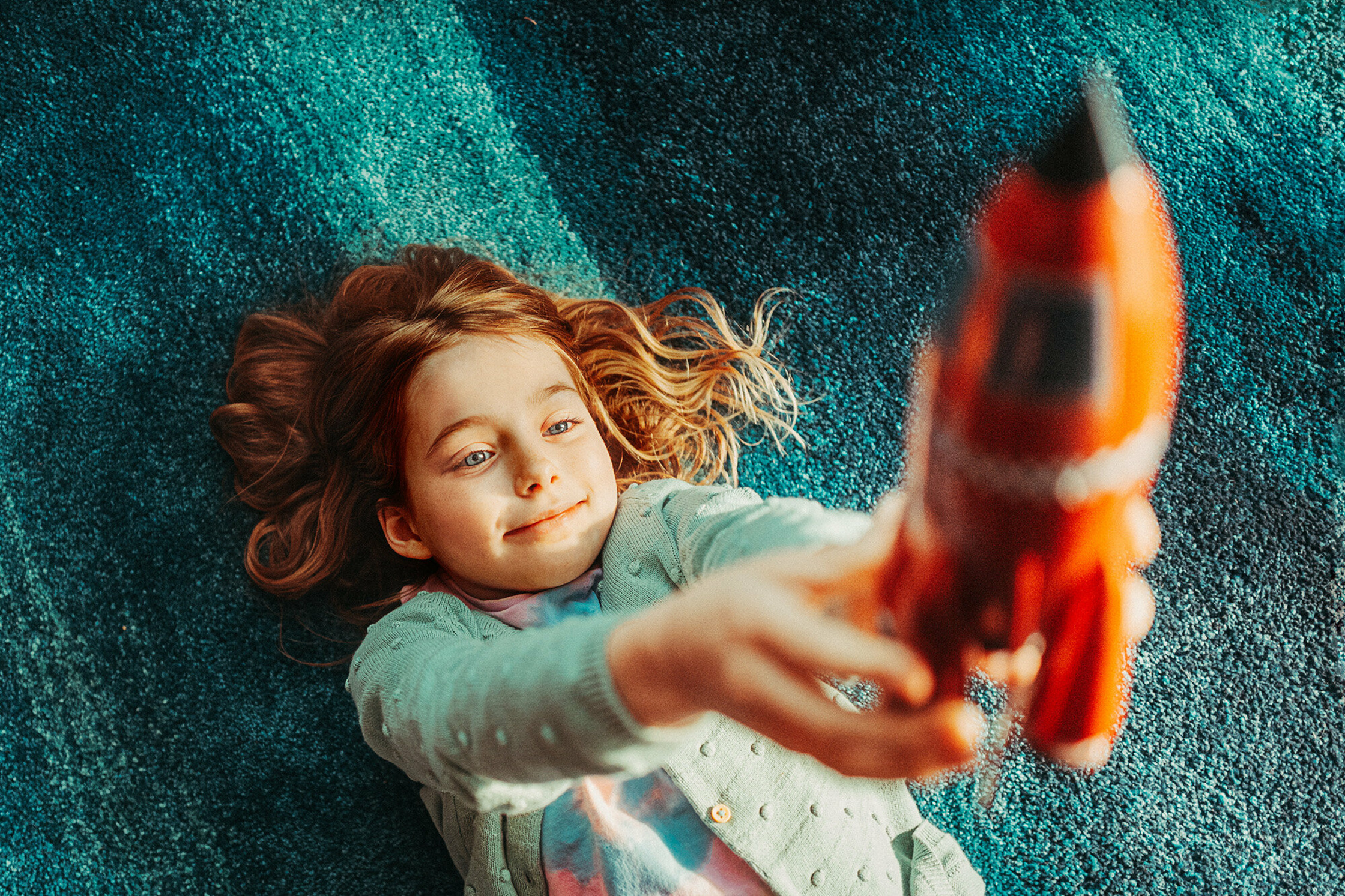 a girl laying on a rug with a toy rocket