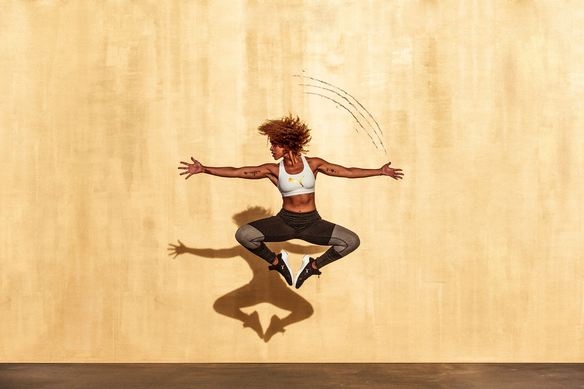 a woman is jumping in the air in front of a wall puma